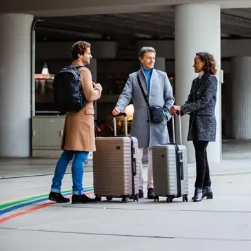 Drei Reisende stehen mit Koffern in einem Parkhaus, umgeben von bunten Linien.