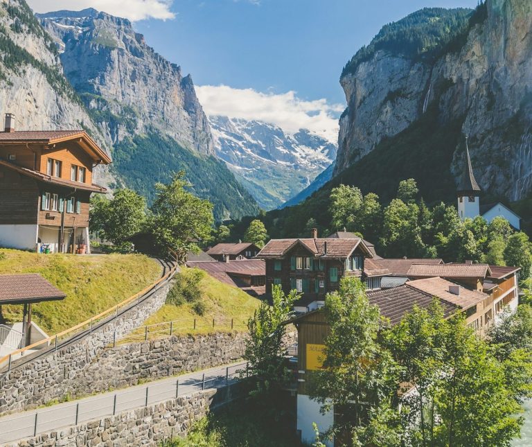 Berglandschaft mit einem Dorf, umgeben von hohen Felsen und schneebedeckten Gipfeln.