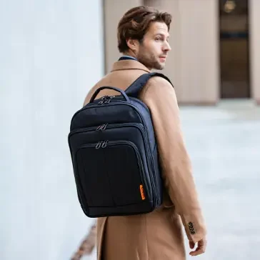 Junger Mann in einem beigen Mantel trägt einen schwarzen Rucksack.
